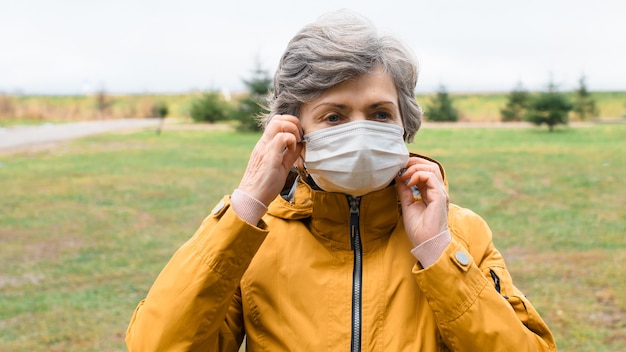 Mulher idosa do retrato tirando a máscara médica. Mulher sênior usando uma máscara protetora do lado de fora em tempo frio.