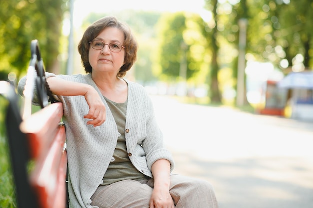 Mulher idosa elegante na camisa está sentada no banco em um parque em um dia quente