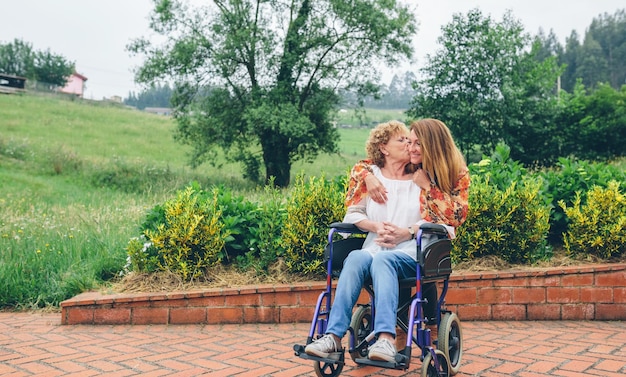 Foto mulher idosa em cadeira de rodas beijando sua filha no jardim