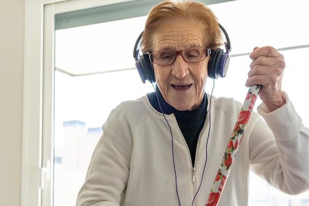 Mulher idosa encantada ouvindo música e fazendo tarefas domésticas