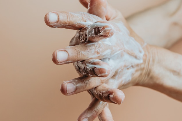 Mulher idosa esfregando creme para as mãos, close-up, mínimo, espaço de cópia de fundo pastel, conceito de autocuidado