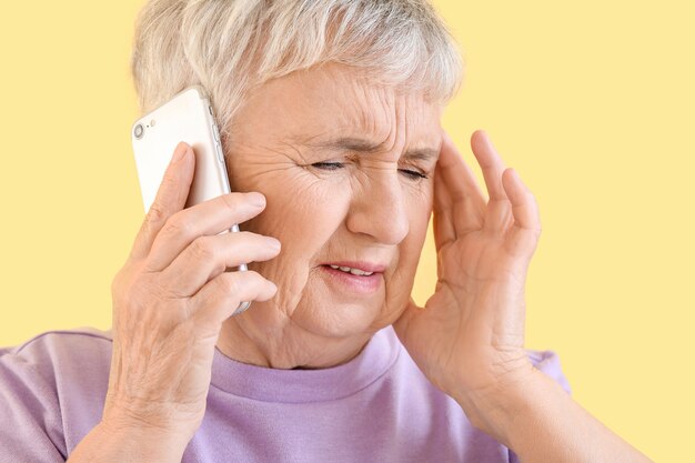 Mulher idosa estressada falando ao telefone no amarelo