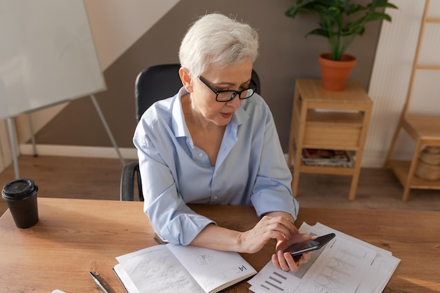 Mulher idosa europeia elegante e confiante de meia idade usando smartphone no local de trabalho elegante e mais velha