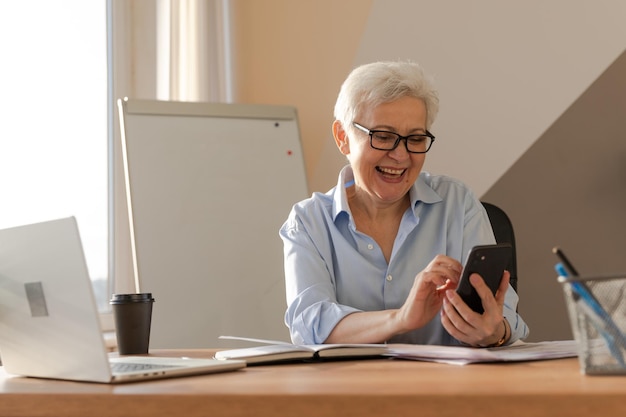 Mulher idosa europeia elegante e confiante de meia idade usando smartphone no local de trabalho elegante e mais velha