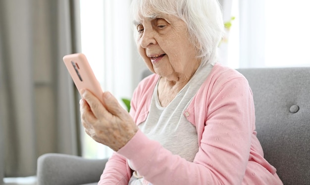 Mulher idosa fala por videochama usando smartphone no quarto de casa