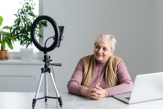 Mulher idosa fazendo videochamada no laptop, acenando para a tela, conversando com crianças, espaço livre.