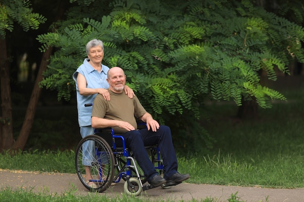 Mulher idosa feliz caminhando com um homem idoso com deficiência sentado em uma cadeira de rodas ao ar livre