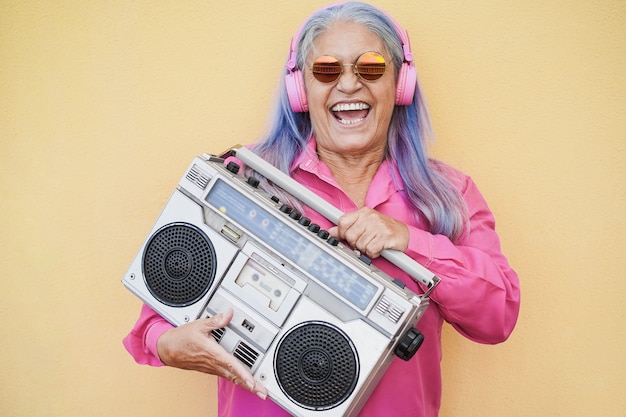 Mulher idosa feliz ouvindo música enquanto segura um aparelho de som vintage boombox - foco no rosto