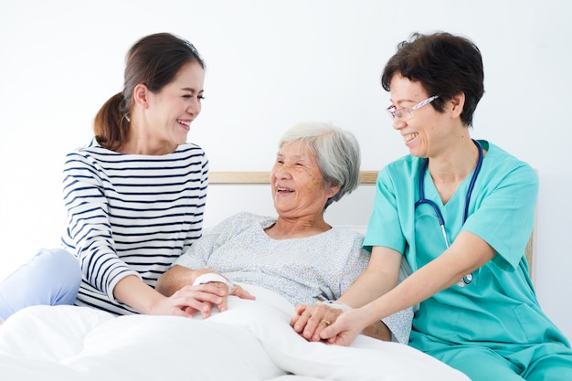 Mulher idosa feliz que fala com enfermeira superior e sua filha na sala de hospital.