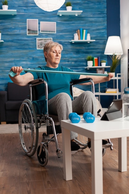 Mulher idosa inválida em cadeira de rodas segurando uma faixa elástica de resistência alongando os músculos do corpo