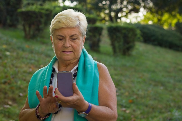 Mulher idosa loira usando telefone inteligente no parque senhora idosa bonita com dispositivo móvel