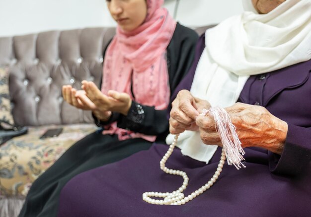 Mulher idosa muçulmana e sua neta usando rosário e orando por Deus