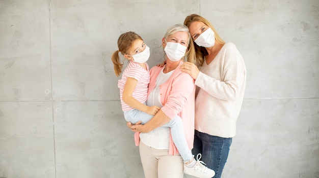 Mulher idosa, mulher adulta e menina bonitinha, três gerações com máscaras faciais protetoras em casa