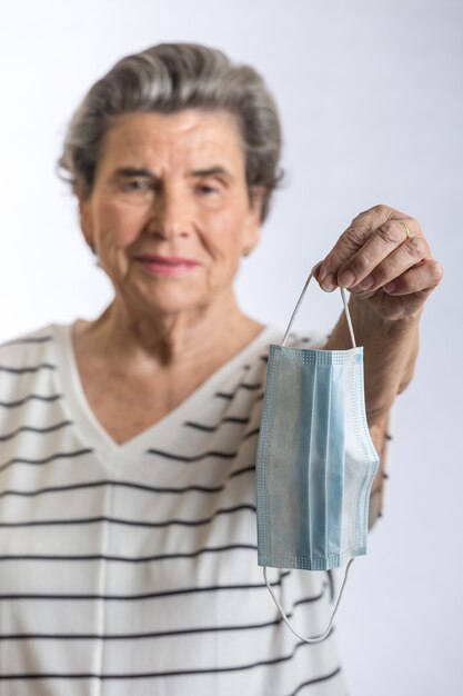 Mulher idosa oferecendo máscara médica para a câmera