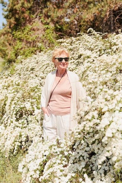 Mulher idosa posando entre arbustos com flores brancas