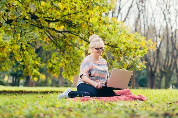 Mulher idosa relaxando no parque com um laptop