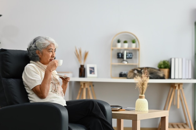 Mulher idosa satisfeita relaxando em uma poltrona e bebendo chá desfrutando de um humor tranquilo e livre de estresse