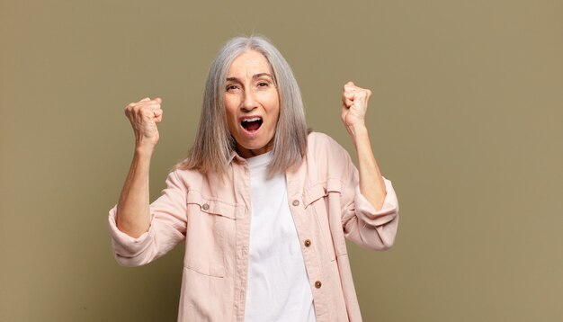 Mulher idosa se sentindo feliz, surpresa e orgulhosa, gritando e comemorando o sucesso com um grande sorriso