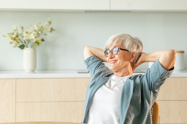 Mulher idosa se sentindo relaxada estendendo os braços na cozinha em casa sorrindo mulher madura estendendo