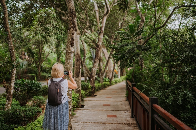 Mulher idosa sênior de mochileiro do viajante andando tirando fotos no parque tropical, natureza de aventura de viagem na China, destino bonito do turista Ásia, viagem de férias de férias de verão, espaço de cópia