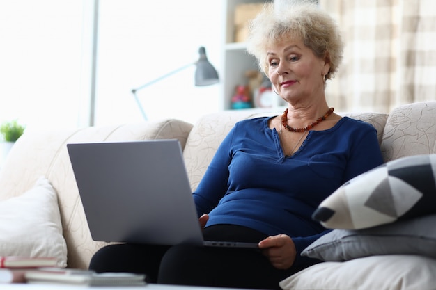 Mulher idosa sentada com o laptop no colo em casa