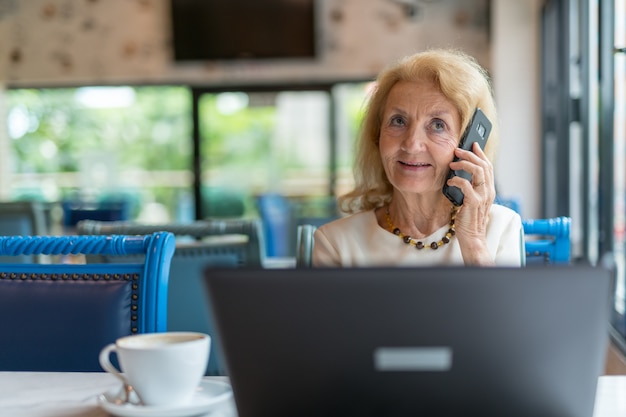 Mulher idosa sentada e usando um laptop e um telefone celular