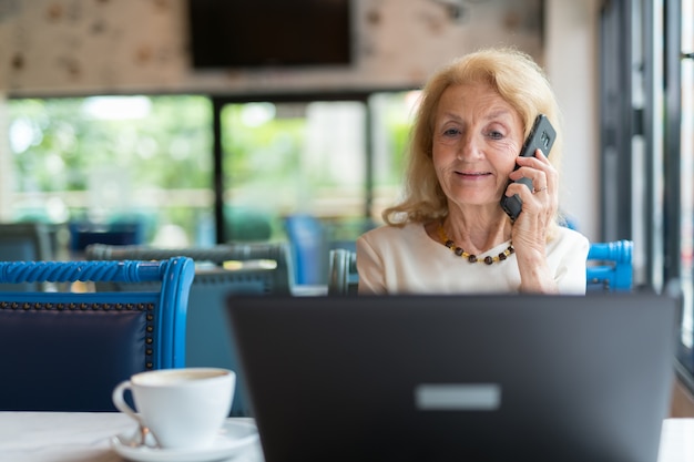 Mulher idosa sentada e usando um laptop e um telefone celular