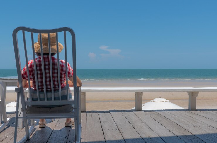 Foto mulher idosa sentada na varanda do hotel olhando para o mar azul e a praia branca em um dia ensolarado