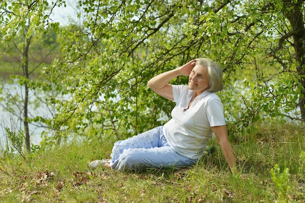 Mulher idosa sentada no verão perto do lago