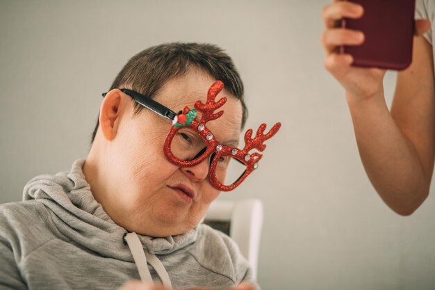 Foto mulher idosa sonolenta com síndrome de down com óculos de natal engraçados chamada de vídeo do telefone