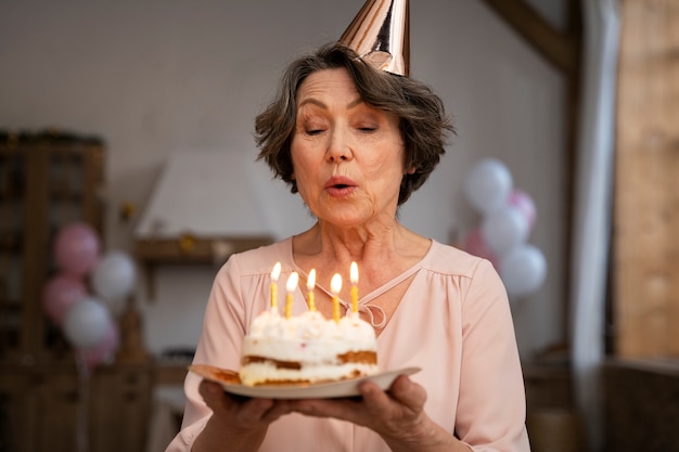 Foto mulher idosa soprando velas e se divertindo na festa