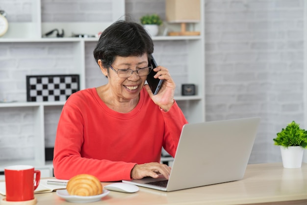 Mulher idosa sorridente ao telefone, falando de negócios, em home office, mulher aposentada trabalhando em casa. Conceito de negócios.