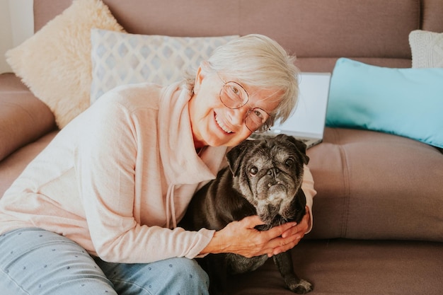 Mulher idosa sorridente atraente e cachorro pug velho engraçado em casa sentado no sofá para retrato de família