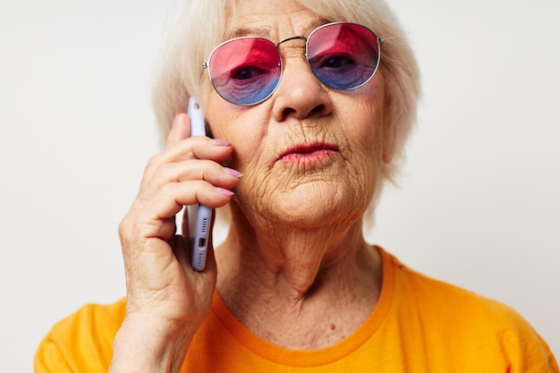 Mulher idosa sorridente em óculos de sol de camiseta casual falando ao telefone emoções fechadas