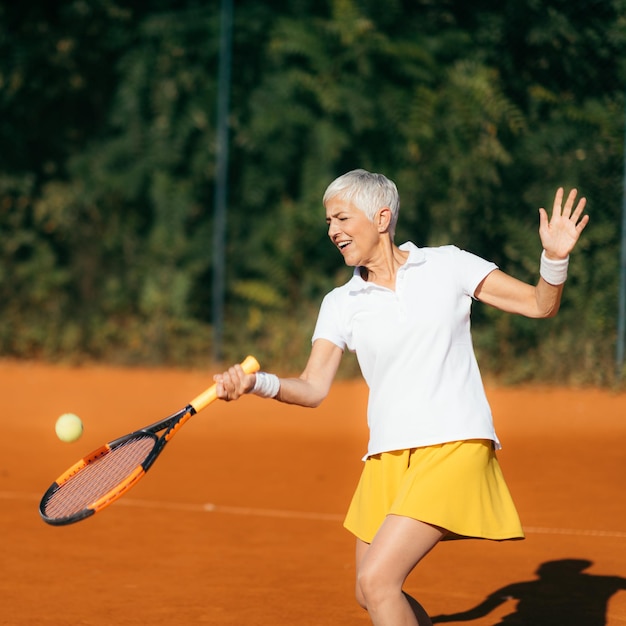 Mulher idosa sorridente jogando tênis como atividade recreativa