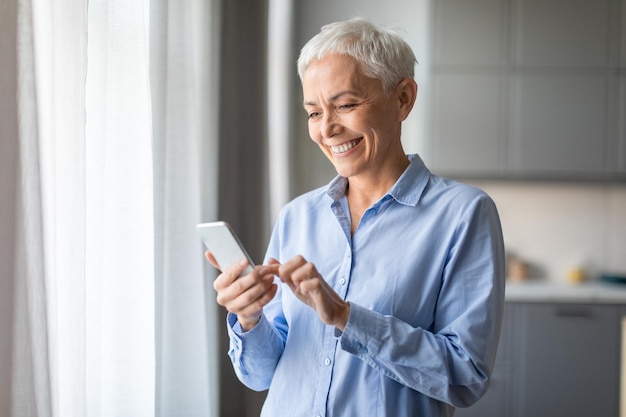 Foto mulher idosa sorridente usando mensagem de telefone celular em casa