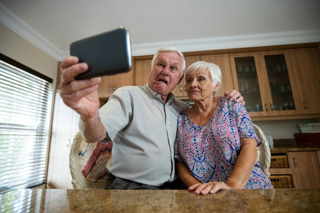 Mulher idosa tirando selfie do celular na cozinha de casa