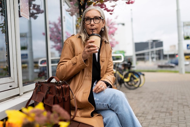 Mulher idosa tomando café sentado em um banco perto da loja