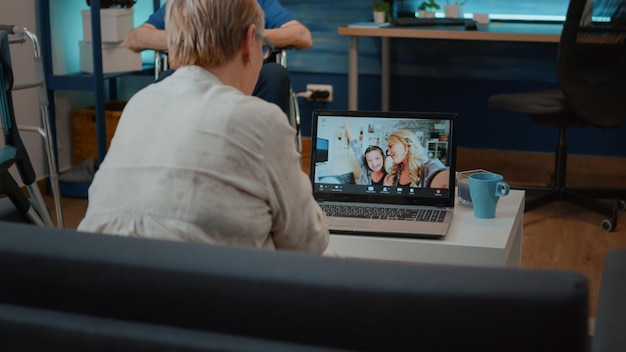 Mulher idosa usando videoconferência remota no laptop, conversando com filha e sobrinha. Pessoa idosa com muletas e deficiência ligando para parentes em teleconferência online. Telecomunicação