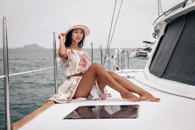 Mulher incrível com pernas longas e sexy, vestindo um vestido de praia e chapéu panamá, está sentada em seu iate privado, retrato