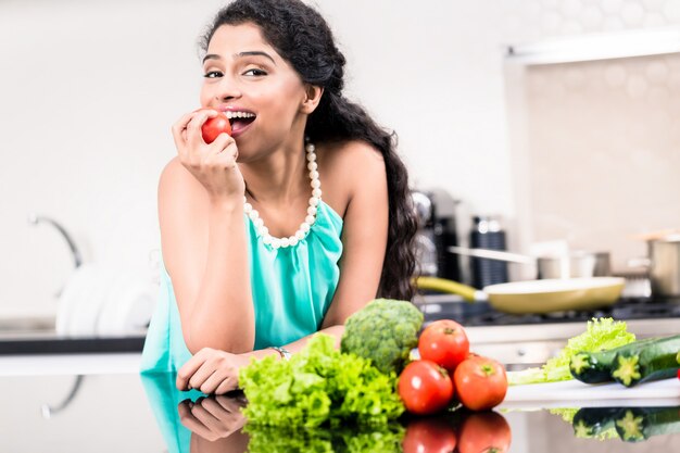 Mulher indiana comendo maçã saudável em sua cozinha