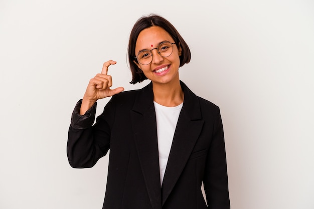 Mulher indiana de negócios jovem isolada no branco segurando algo pequeno com os indicadores, sorrindo e confiante.