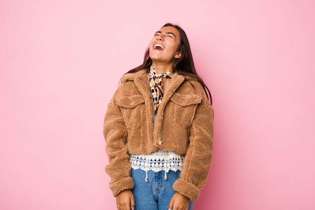 Mulher indiana de raça mista jovem vestindo uma pele de carneiro curta coatrelaxada e feliz rindo, pescoço esticado, mostrando os dentes.