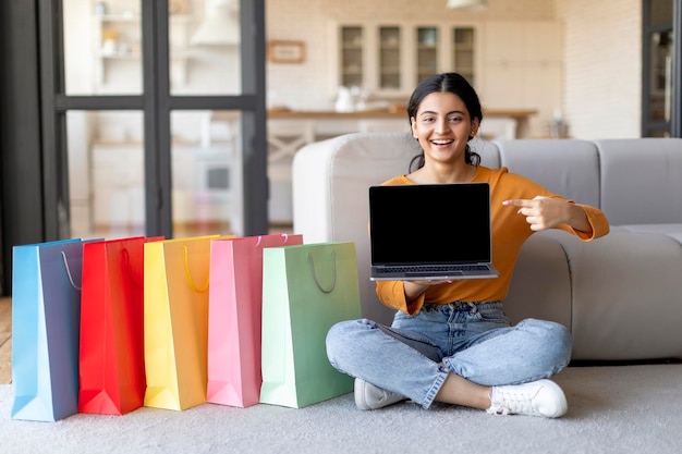 Mulher indiana feliz de compras on-line apontando para laptop com tela em branco