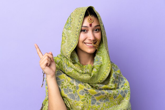 Mulher indiana isolada no fundo roxo feliz e apontando para cima