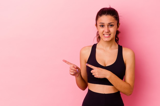 Mulher indiana jovem esporte isolada na parede rosa chocada apontando com o dedo indicador para um espaço de cópia.