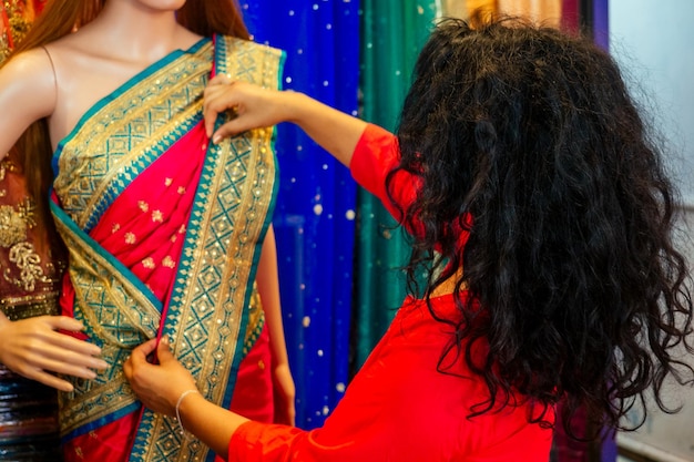 Mulher indiana morena escolhendo uma nova tradição saree no vestido de tecido de cortina de designer de agulha de mercado em um manequim