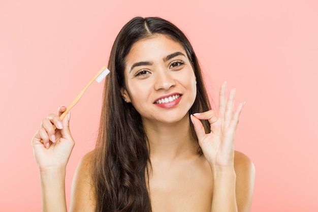 Mulher indiana nova que mantém uma escova de dentes alegre e segura mostrando o gesto aprovado.