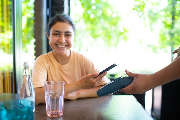 Foto mulher indiana paga com terminal de pagamento sem contato de nfc de telefone móvel no café bar.