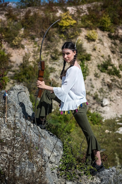 Mulher indiana posa em uma natureza ao redor com flecha e arco